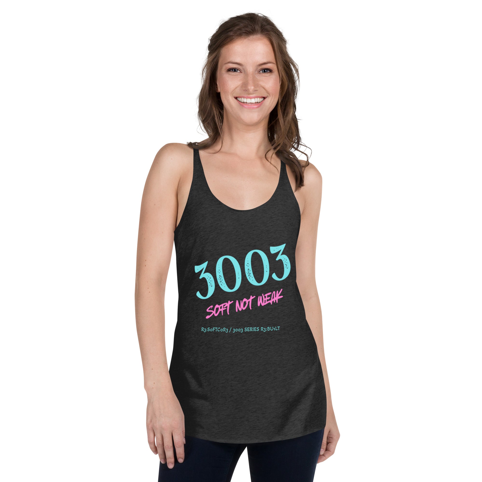 A woman modeling a dark charcoal racerback tank top with a graphic that reads '3003 SOFT NOT WEAK' in teal and pink.